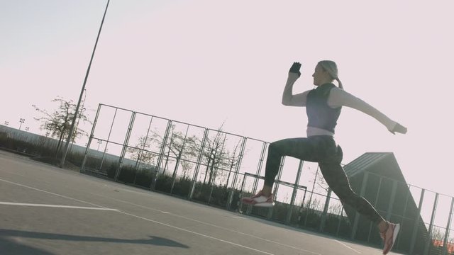 Energetic athletic woman bounding on a fenced court in residential area. Shot in slow motion early in the morning at sunrise.