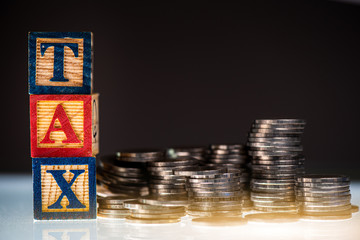 Stack of coins with TAX text on black background, money for tax payment concept