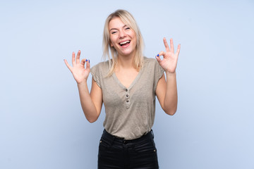 Fototapeta na wymiar Young blonde woman over isolated blue background showing an ok sign with fingers