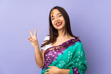 Young Indian woman isolated on purple background smiling and showing victory sign