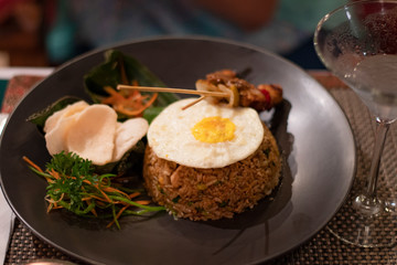Nasi goreng, a traditional balinese food served during the dinner in a black plate with cocktail drink in a restaurant in Bali