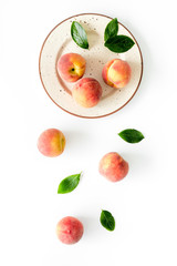Red peaches pattern with plate and leaves on white table top-down