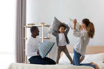 Happy African American family playing pillow fight on bed
