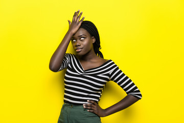 Tired girl covers face with hand, stress. Young african american girl wears casual outfit on yellow background. Emotions and Omg concept