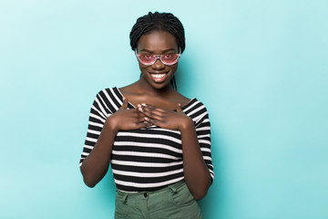 Headshot of pleased touched young African American woman smiles gently, feels pleased, wears striped top and headwear, isolated over blue background. People, happiness and emotions concept