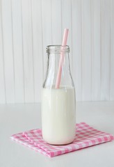 Little rustic milk bottle with straw on pink checked napkin. Milk for kids, white wooden background.