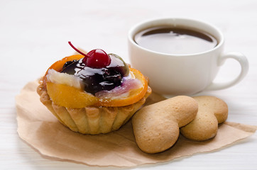 basket cake decorated with different fruit and cup of coffee on white table
