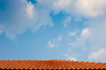 Bright light blue sky with many white and grey chunks of clouds floating background, with red brown concrete wavy corrugated roof as the lower border