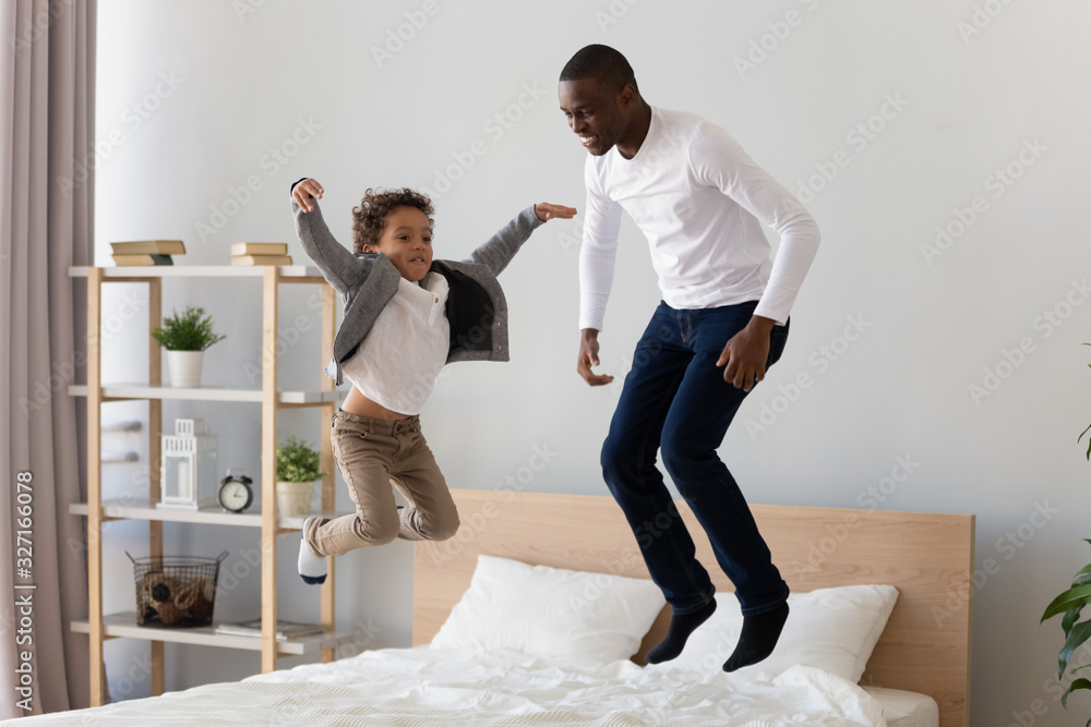 Wall mural happy african american father and little son jumping on bed