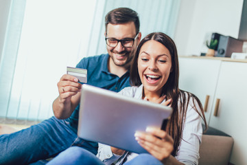 Smiling happy couple with tablet pc computer and credit or bank card shopping online at home