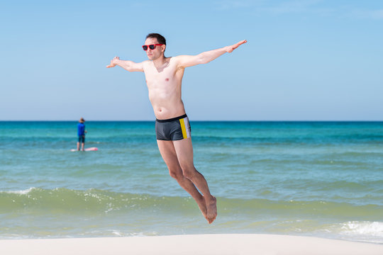 Young man jumping by ocean water mid-air with arms outstretched in summer in Santa Rosa Beach, Florida flying with boat in background