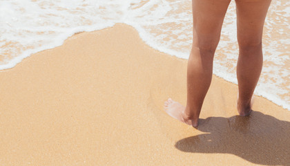 Closeup of a woman bare feet standing at sandy beach, with a wave foaming - travel and relaxing.