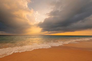 Fototapeta na wymiar Waves on sandy ocean beach under a beautiful sunset sky with clouds on Sri Lanka island.
