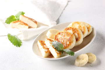 Concept of Russian and Ukrainian cuisine. Cottage cheese pancakes. Cheesecakes with banana and mint on a white background. Background image, copy space