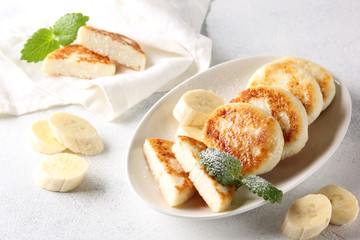 Concept of Russian and Ukrainian cuisine. Cottage cheese pancakes. Cheesecakes with banana and mint on a white background. Background image, copy space