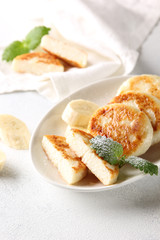 Concept of Russian and Ukrainian cuisine. Cottage cheese pancakes. Cheesecakes with banana and mint on a white background. Background image, copy space