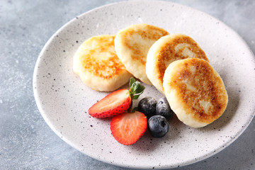 Concept of Russian and Ukrainian cuisine. Cottage cheese pancakes. Cheesecakes with fresh berries on a light grey background. Background image, copy space