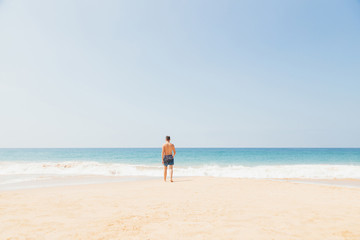 Teenage boy, walking into the water, at the ocean sandy beach. Travel and vacation concept.
