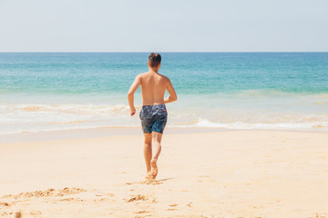 Teenage boy, running into the water, at the ocean sandy beach. Travel and vacation concept.