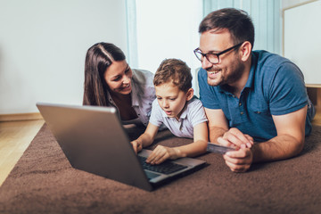 Obraz premium Beautiful parents and their son are doing shopping online using laptop and smiling at home.