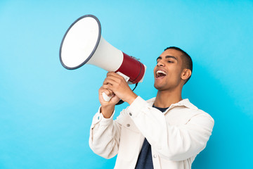 Young African American man over isolated blue background shouting through a megaphone