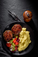 burger with mashed potatoes and vegetables salad on a black plate on Dark grey black slate background