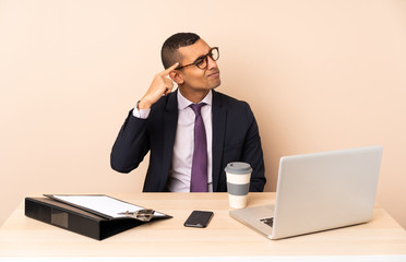 Young business man in his office with a laptop and other documents making the gesture of madness putting finger on the head