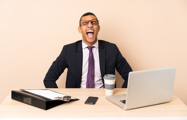 Young business man in his office with a laptop and other documents shouting to the front with mouth wide open