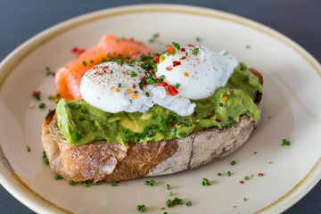 Poached eggs on top of smashed avocado on sourdough toast with smoked salmon. Healthy breakfast with plate on table. Close up, shallow depth of field.
