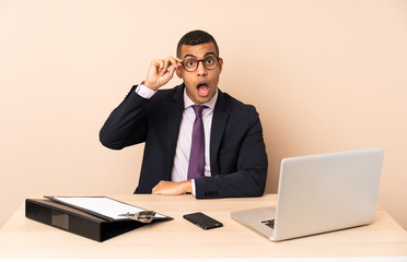 Young business man in his office with a laptop and other documents with glasses and surprised
