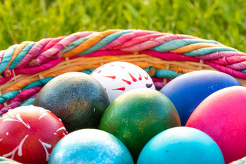 Detail on a colorful Easter eggs in a wicker basket with a green grass background
