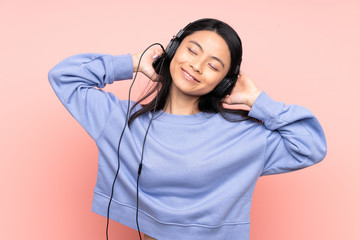 Teenager Chinese girl isolated on pink background listening music