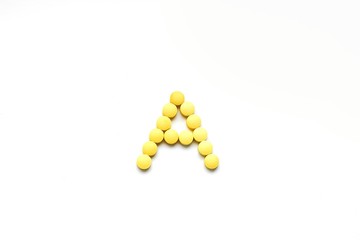 The concept of pills vitamins for treatment. Group A vitamin is laid out by yellow pills on a white isolate background. Water soluble vitamins. Lipovitamins. The complex of vitamins. Copy space.