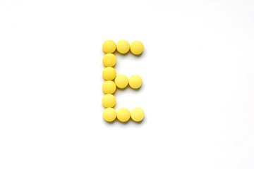 The concept of pills vitamins for treatment. Group E vitamin is laid out by yellow pills on a white isolate background. The complex of vitamins. Copy space. Place for text.