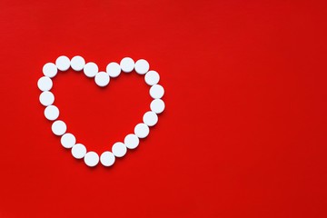  Concept of heart pills. Small white pills scattered in the shape of a heart on a red background....