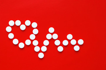Pills concept for heart and cardiovascular disease. White pills form a cardiogram and heart symbol...