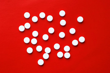 The concept of pills for treatment. White pills are scattered on a bright red background. Copy space. Isolated background.