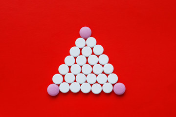 The concept of pills for treatment. White and pink pills on a bright red background in the form of a triangle or pyramid. World order in medicine. Copy space. Isolated background.