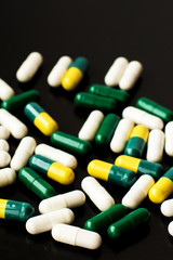 Medicine concept. Green and yellow pills on a black isolated background. Medicines for diseases, medical care. Place for text. Copy space. Isolated background.