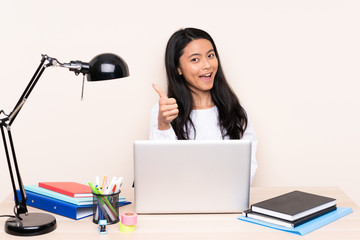Student asian girl in a workplace with a laptop isolated on beige background with thumbs up because something good has happened