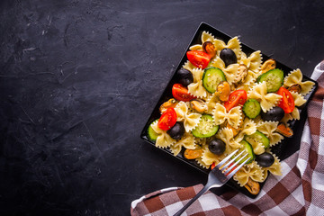 tasty pasta salad with tomato cucumber and olives on a dark stone background