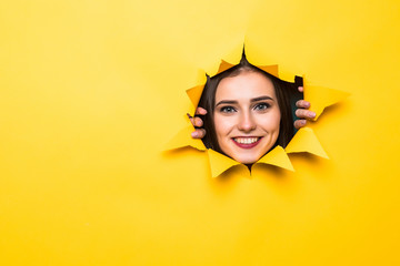 Glad young man with toothy smile looks positively aside, shows face in paper hole, isolated over yellow background with blank space. Positive emotions. Man peeks through ripped paper