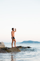 Young man standing on the rock enjoying the sunset by the sea
