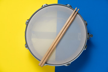 Drum stick and drum on yellow and blue table background, top view, music concept
