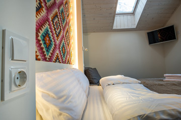 Interior of a spacious hotel bedroom on attic floor with fresh linen on a big double bed. Cozy contemporary mansard room in a modern house.
