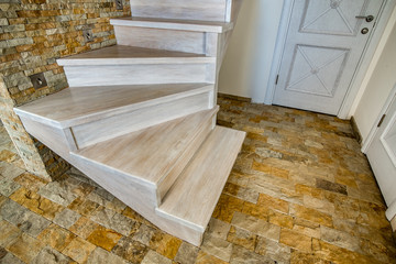 Stylish wooden contemporary staircase inside loft house interior. Modern hallway with decorative limestone brick walls and white oak stairs.