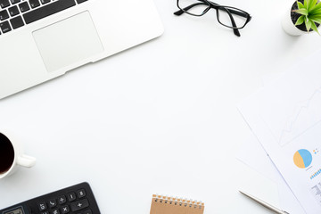 White business office desk table with laptop computer, business graph documents and supplies. Top view with copy space, flat lay.