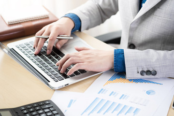 Young businessman is typing the business performance results on laptop computer keyboard. Online financial data analyzing concept.