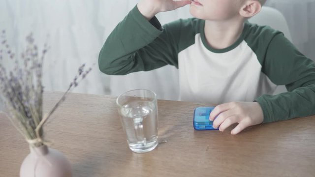 The boy albino eats medicine and washed it down with water at home at the table.