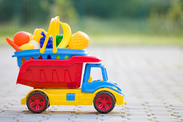 Bright plastic colorful toy car truck carrying basket with toy fruits and vegetables outdoors on...